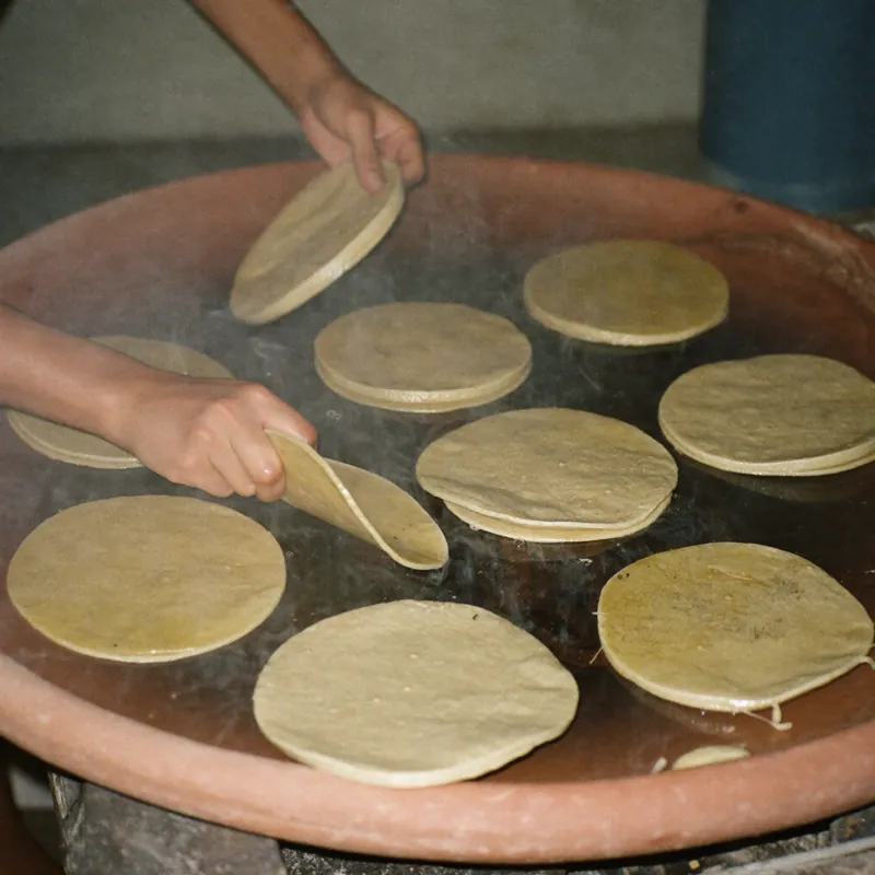 Manos echando tortillas de maíz en el comal de barro
