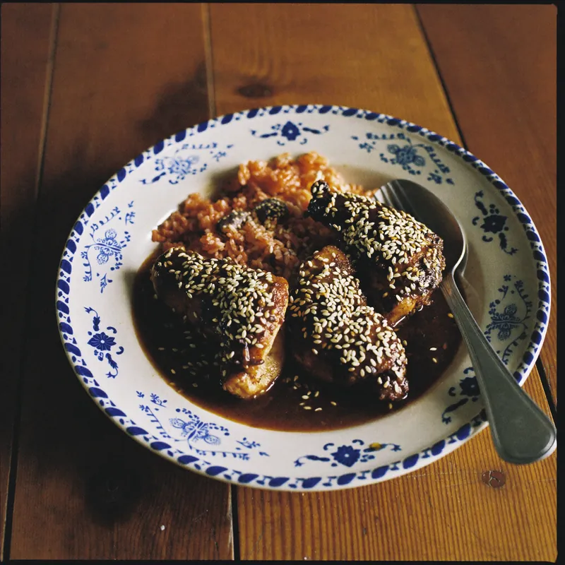 Pollo en mole poblano con ajonjolí y arroz rojo en plato de talavera