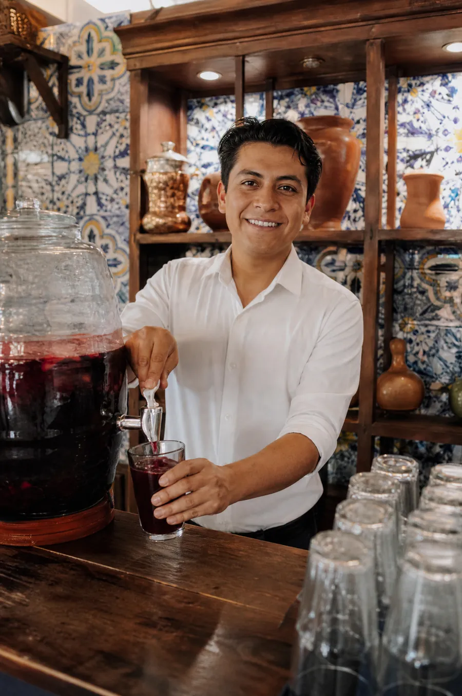 Tomás sirve agua de jamaica desde la vitrolera, detrás de la barra